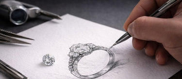 Hand drawing a diamond ring on paper with jewelry tools in the background